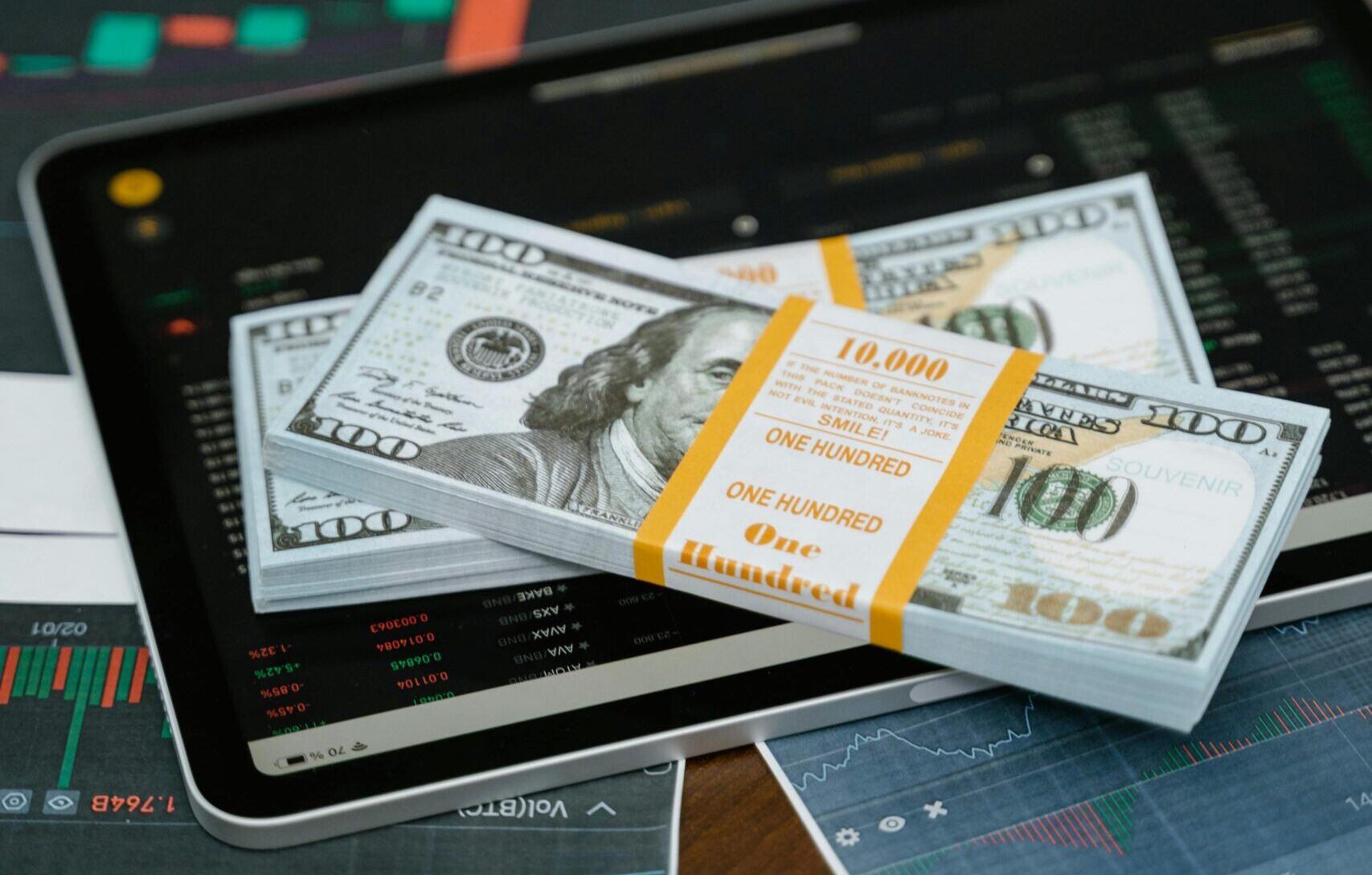 Stack of $100 bills placed on a tablet with financial graphs, symbolizing digital finance.